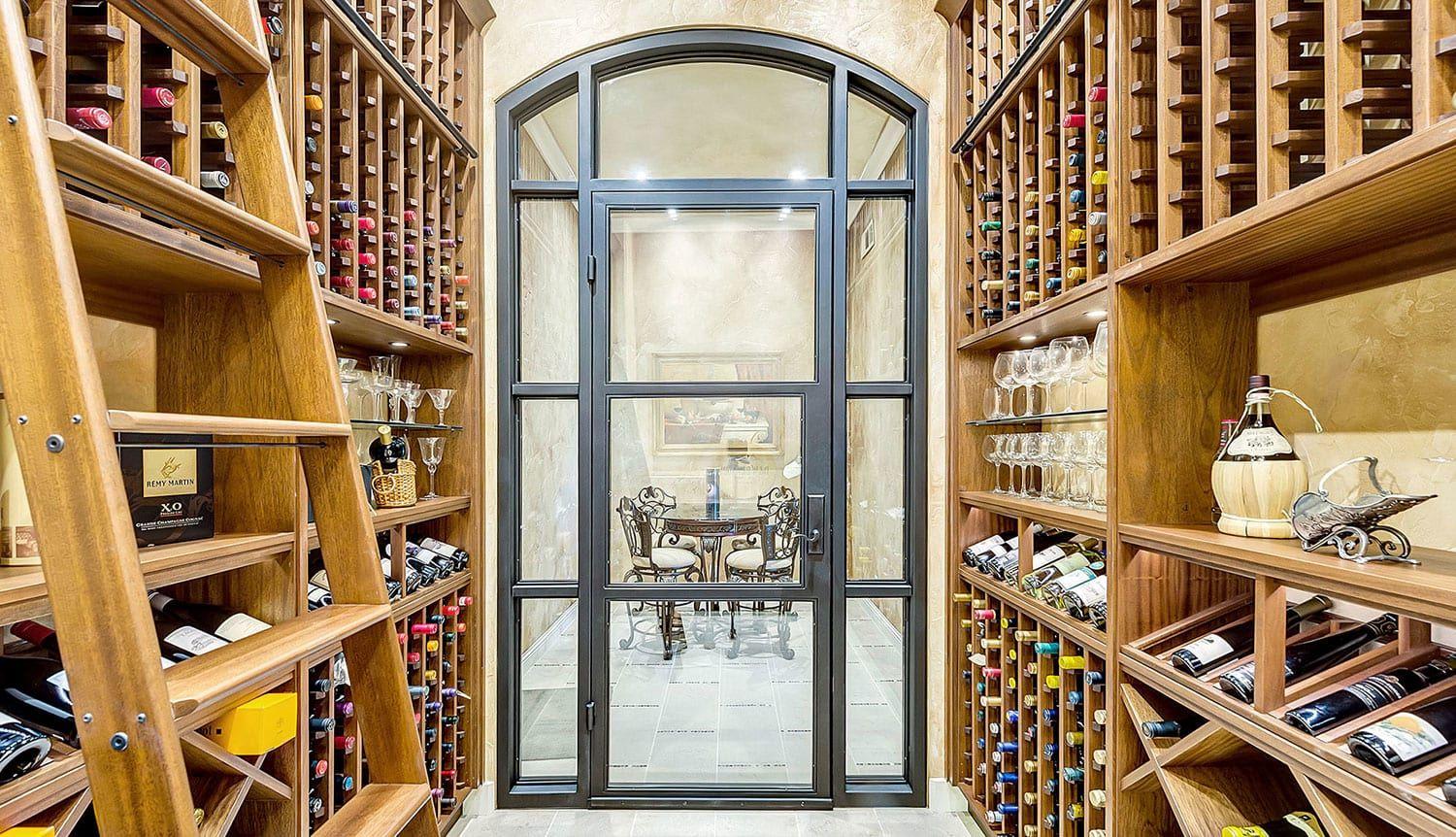 Stunning wood wine cellar custom made for a Texas home with a dramatic arched window and ladder.